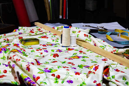 Sewing workshop with a table full of fabrics of various colors and patterned textures, ready for cutting and makingの写真素材