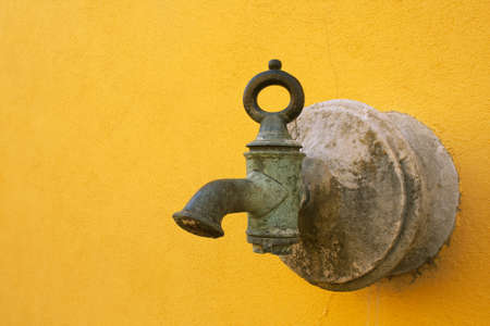 Ancient faucet in bronze in a yellow wallの写真素材