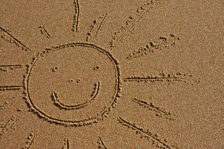 Smiling face of the sun drawn in the sandの写真素材