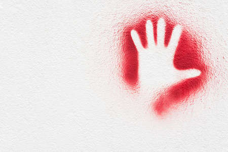 Clipping of an open hand print in a red ink stain, on a white wallの写真素材