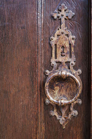 Old metal lock knocker, with a christian cross, on a door of woodの写真素材