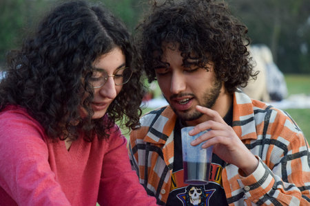 Young couple sitting in the park and drinking water from a glass.の写真素材