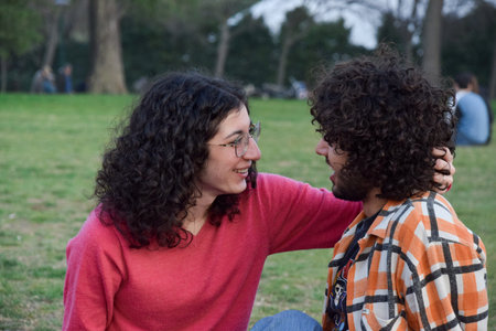 Young couple sitting in the park and talking, looking at each otherの写真素材