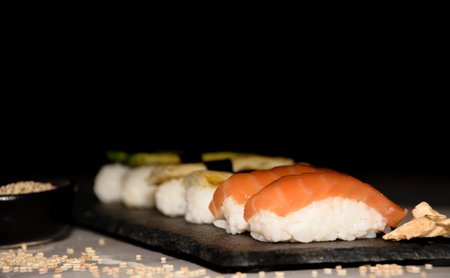 Sushi on a black background with chopsticks and sesame seedsの写真素材