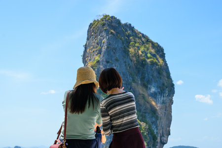 Couple of Asian girls taking a photo of a friend on the beach with an island in the backgroundの写真素材