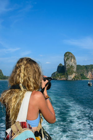 Young blonde woman taking a photo to an island from the deck of a boatの写真素材