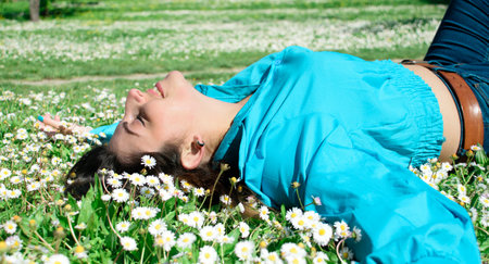 Beautiful young woman with marguerite lying on green grass in park.の写真素材