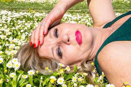 Mature woman lying in grass with margheritesの写真素材