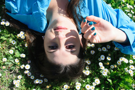 Beautiful young woman with marguerite lying on green grass in park.の写真素材