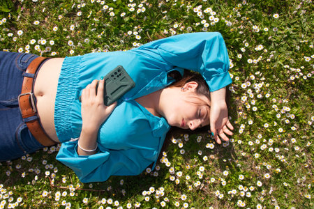 Beautiful young woman lying on green grass with cell phoneの写真素材