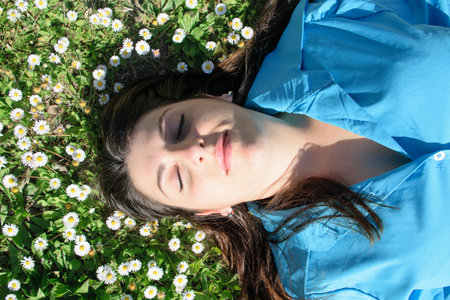 Beautiful young woman with marguerite lying on green grass in park.の写真素材