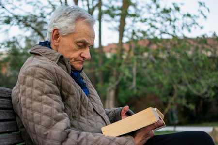 Old man with gray hair reading a book sited on an bench.の写真素材