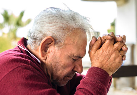 Old man with red sweater and gray hair praying with his hands in supplication.の写真素材