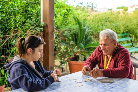 Grandfather playing cards with his granddaughter outdoors in garden.の写真素材