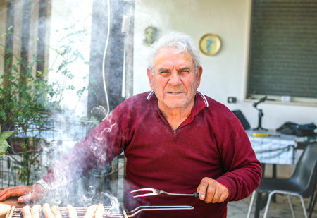 Grandfather cooking on barbecue outdoors in gardenの写真素材