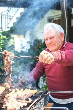 Grandfather cooking on barbecue outdoors in gardenの写真素材