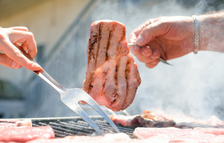 Hand holding steak cooking on smoking barbecue on terrace.の写真素材