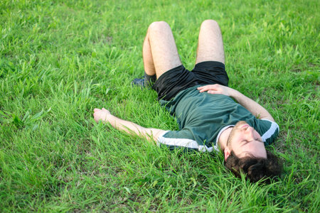 Young man with green t-shirt lying on grass in park after exercising exhausted
