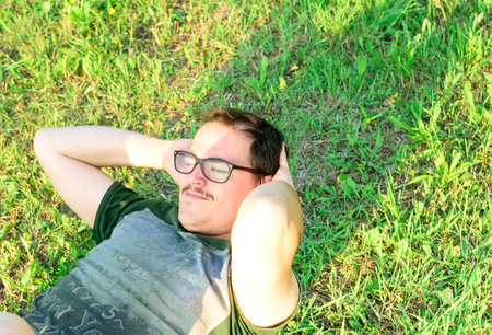 Young man with glasses and green t-shirt doing sit-ups and exercising in parkの写真素材