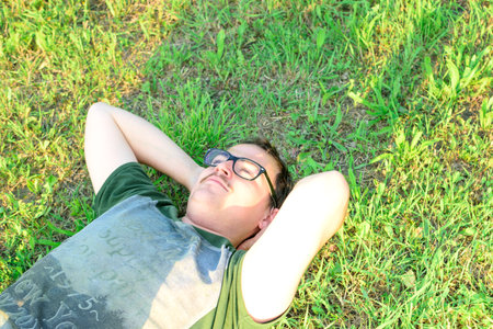 Young man with glasses lied on grass enjoying vacation after studying very happy