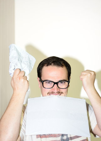 Man with glasses raising his hands and biting papers angry from stress of work