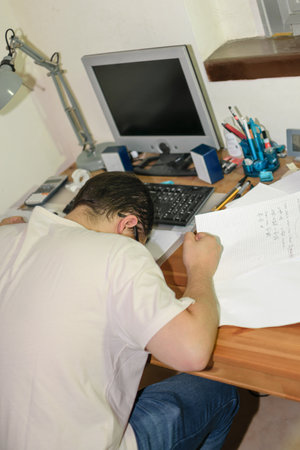 Young man with glasses with his head on desk on top of papers stressed by his studies