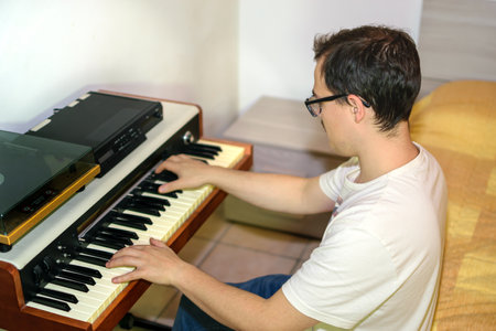 Young man with glasses and white t-shirt composing and playing piano in his bedroomの写真素材