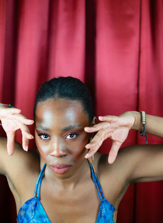 African Woman with blue dress dancing in red background looking deeply with hands