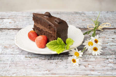 slice of chocolate cake on a white vintage plate on a wooden table with cracked paintの写真素材
