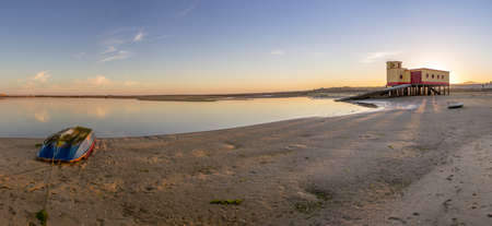Sunset and historic lifeguard building in the foreground at Fuseta fishing town Ria Formosa conservation park Algarve. Portugalの写真素材
