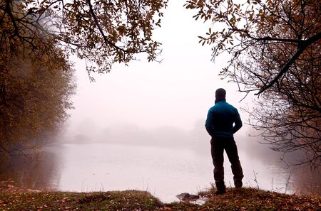 Man in foot to the shore of a lake covered by a dense fogの写真素材