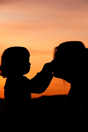 Silhouettes at sunset of a mother and her daughter showing her affection and tenderness - Vertical  2の写真素材