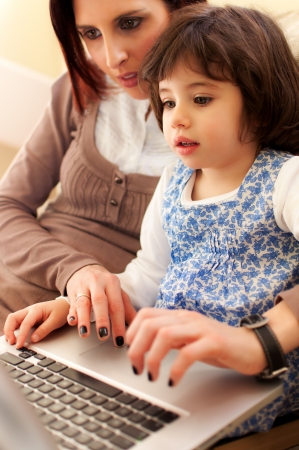 Mother and daughter amuse themselves playing cabbage the computer in the sofa of house - Verticalの写真素材