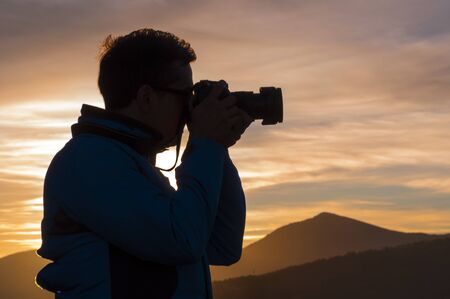 Silhouette of photographer taking photo at sunset of a mountainous landscape