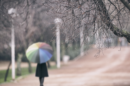 Woman in the rain at the park with a colorful umbrellaの写真素材