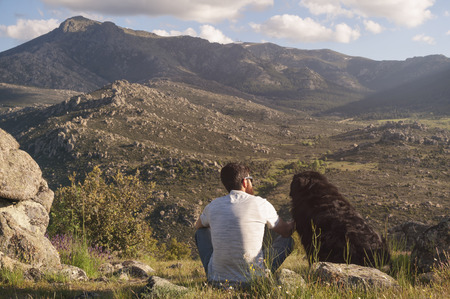 Young man and his dog enjoying the sunset sitting together at the top of the mountainの写真素材