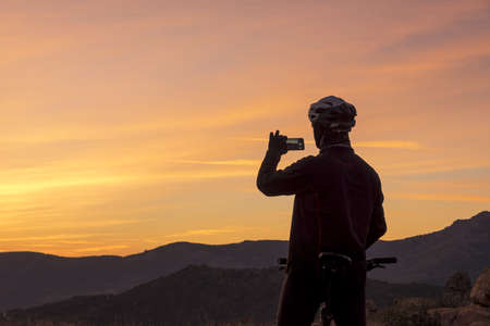 Man taking sunset sky picture on the mountain at sunsetの写真素材