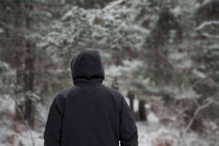 Young man in warm clothing and hat walking in winter forestの写真素材