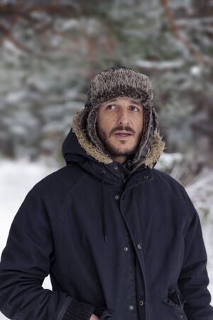 Young man in warm clothing and hat walking in winter forest