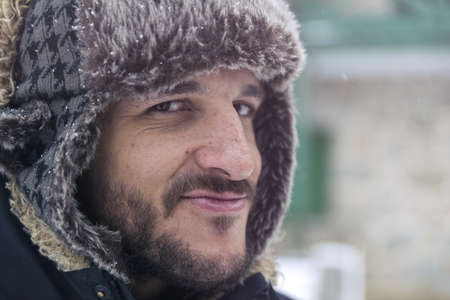 Young man in warm clothing and hat walking in winter forestの写真素材