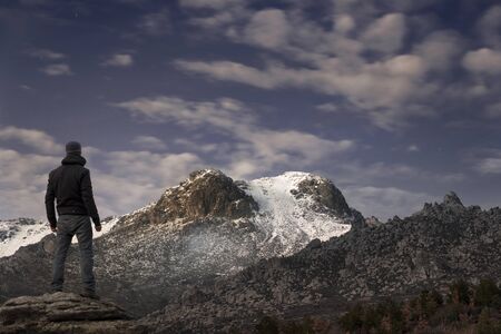Man contemplates the last rays of the sun on the snowy mountain at sunsetの写真素材