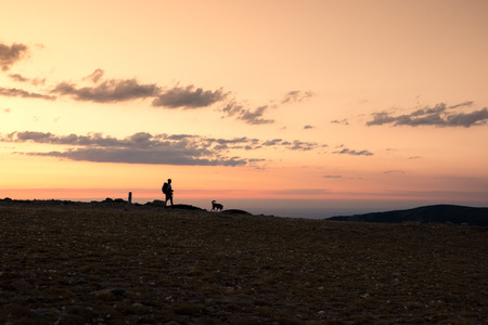 Hiker and his dog walk down the mountain in an amazing sunset. Navacerrada, Spain.の写真素材