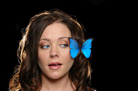 Beautiful girl with butterfly on her face against a black blackgroundの写真素材