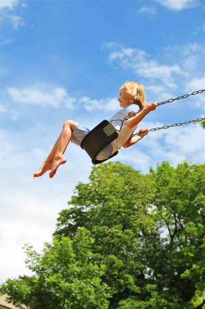 Little girl swinging on a sunny day with trees in the backgroundの写真素材
