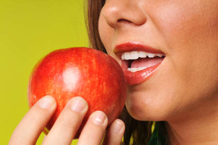 Young woman eating a red apple against a green backgroundの写真素材