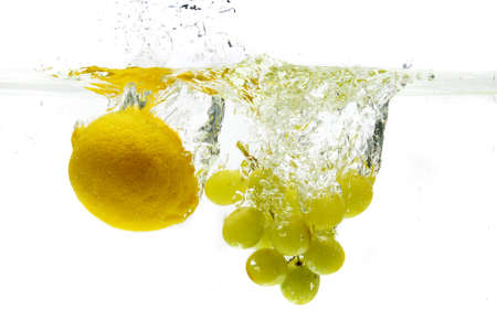Lemon and grapes dropped in the water isolated against a white backgroundの写真素材