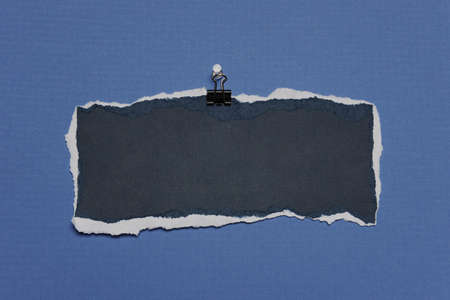 Piece of Rip Paper with white edges on a clip against a blue backgroundの写真素材