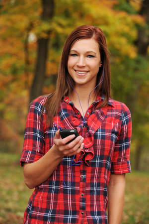 Young Woman listening to music with headphones and fall bacground out of focus