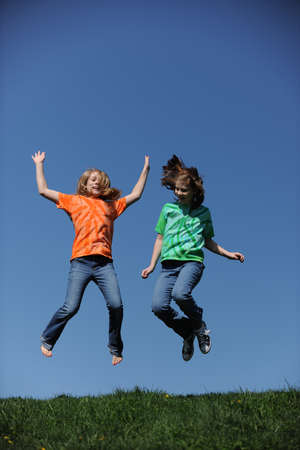Two young Girls jumping on a sunny day against a blue skyの写真素材