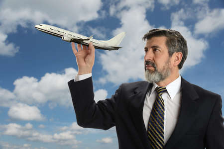 Mature Businessman holding a plane with clouds and sky as backgroundの写真素材